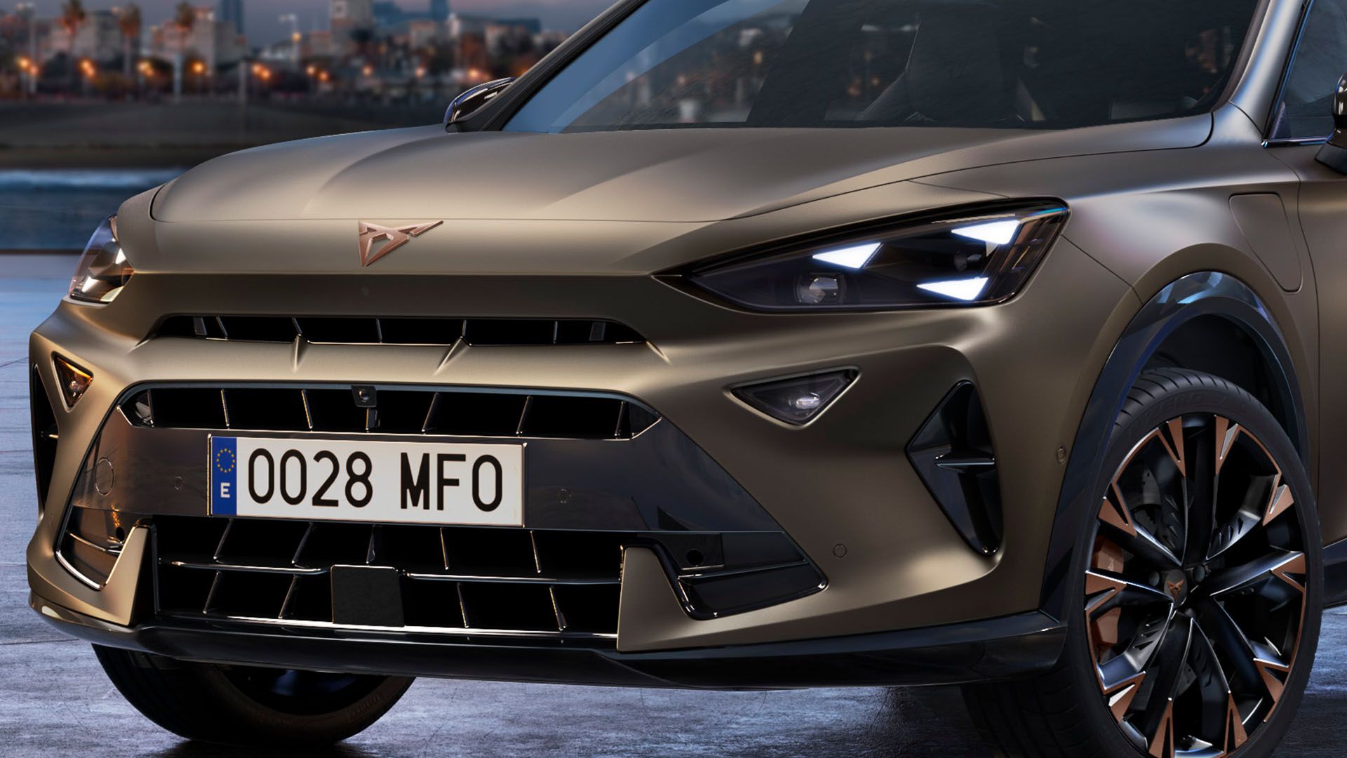 Detailný pohľad na prednú časť hnedého moderného SUV. Auto má špz s číslom 0028 MFO a elegantné LED svetlomety. V pozadí je rozmazané mestské prostredie.