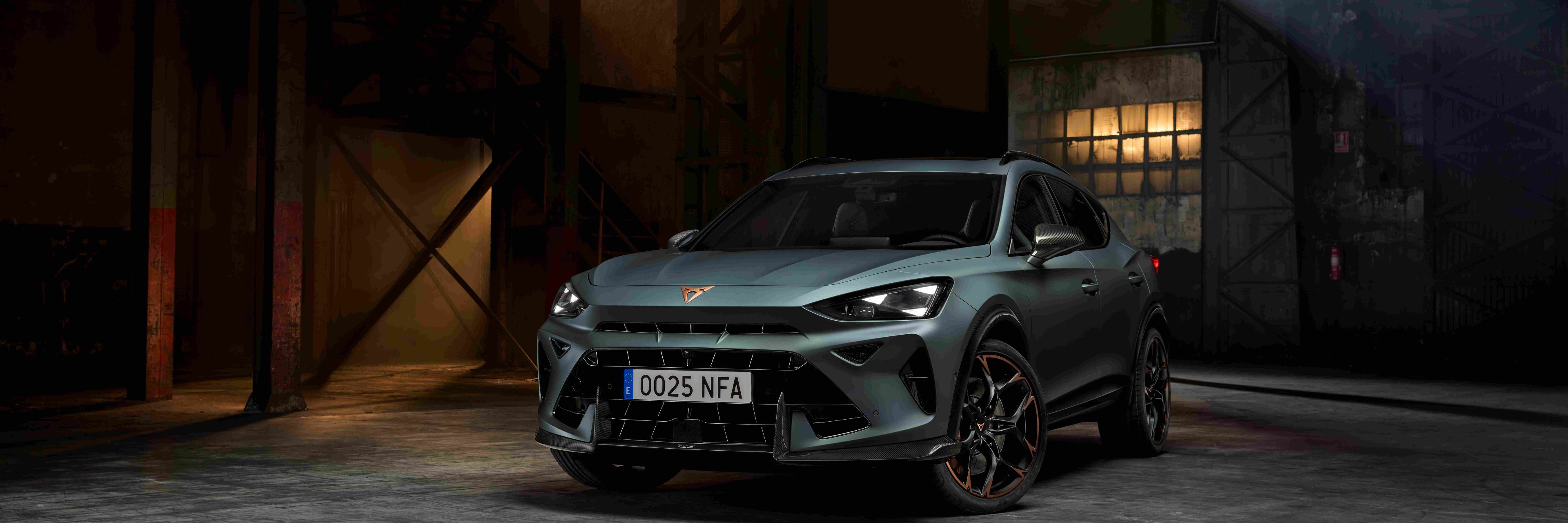 CUPRA Dormentor v zelenej farbe stojí v industriálnom prostredí s nepriamym osvetlením. Športový vzhľad auta podčiarkujú výrazné svetlá a aerodynamické línie. 