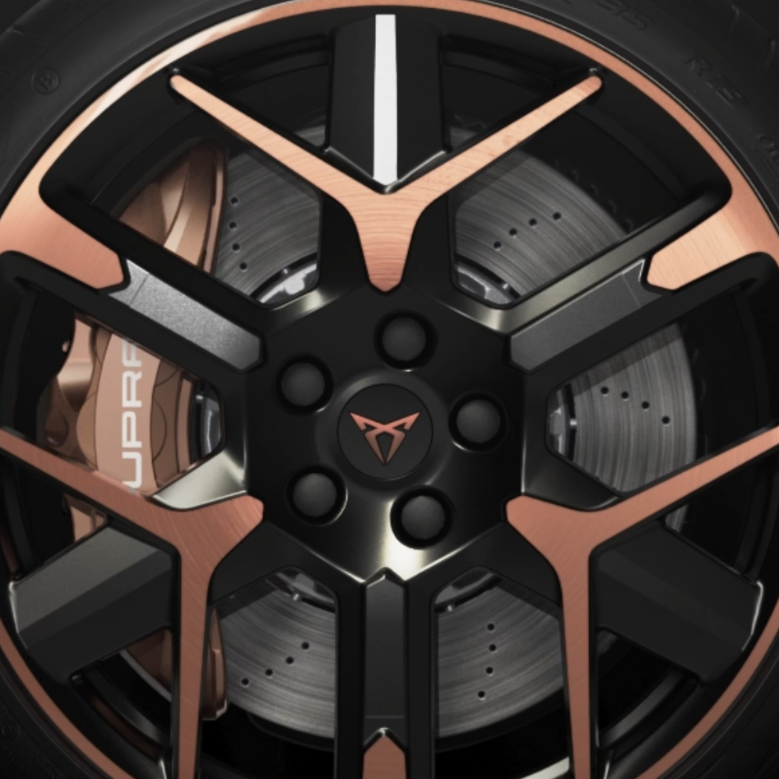 Detailný záber na koleso automobilu, zložené z čierneho disku s bronzovými prvkami. Perforovaný brzdový kotúč a nápis "Cupra" na brzdovom strmeni sú viditeľné.