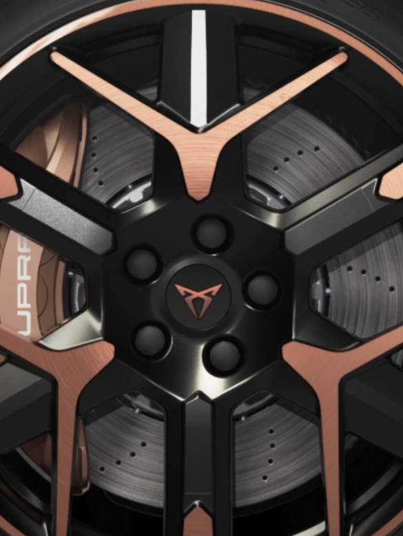 Detailný záber na koleso automobilu, zložené z čierneho disku s bronzovými prvkami. Perforovaný brzdový kotúč a nápis "Cupra" na brzdovom strmeni sú viditeľné.