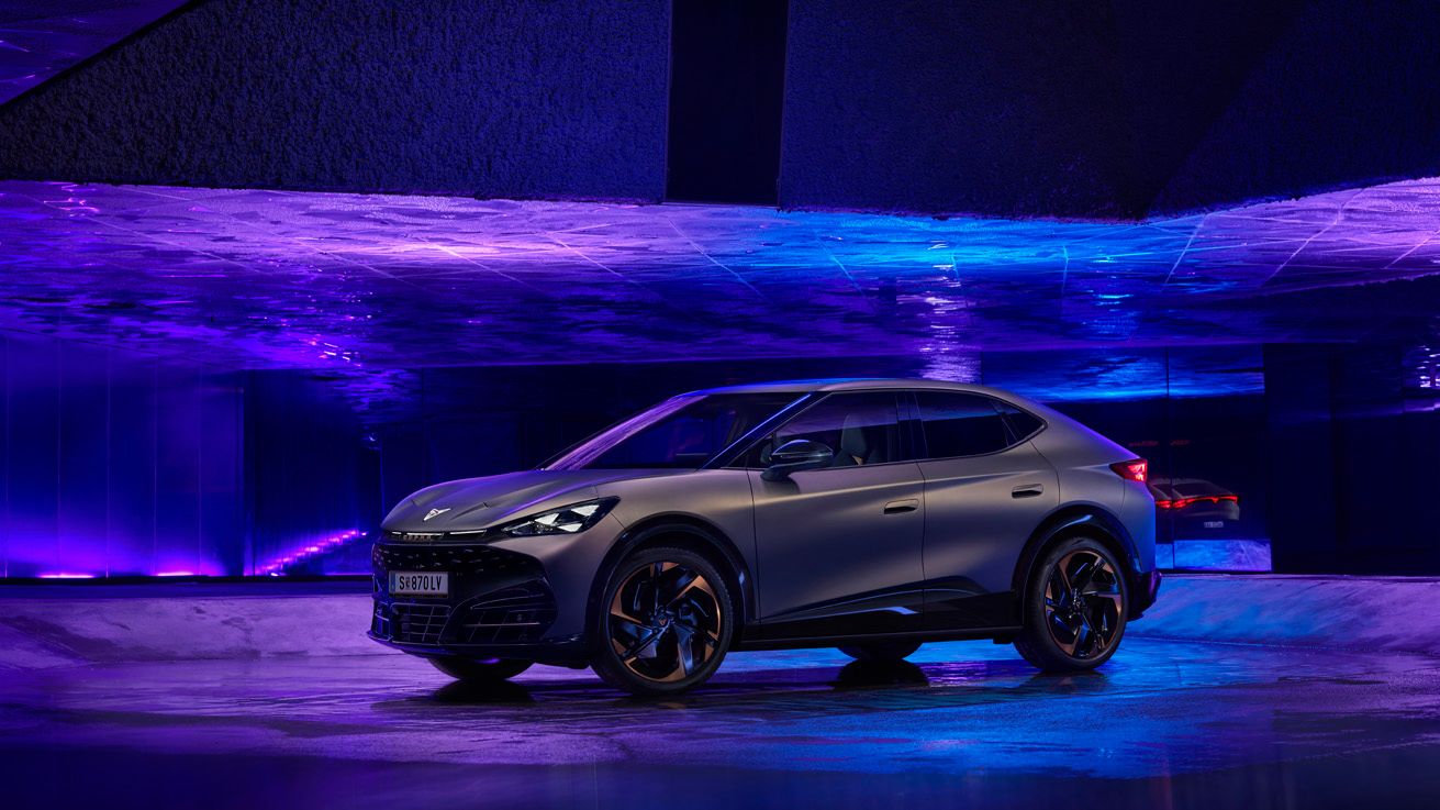 Tmavosivé moderné CUPRA Tavascan je zaparkované v osvetlenom podzemnom priestore s fialovým a modrým osvetlením. Jeho dizajn je športový a aerodynamický. Pozadie pôsobí futuristicky.