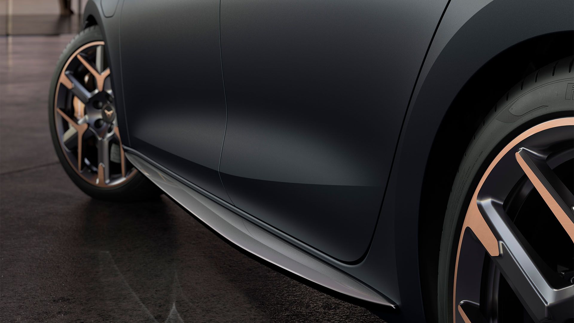 Detailný záber na bočnú časť vozidla, zobrazujúci jeho moderné kolesá s unikátnym dizajnom. Tmavosivý odtieň dodáva vozidlu elegantný vzhľad. Vozidlo je zaparkované na betónovom povrchu.