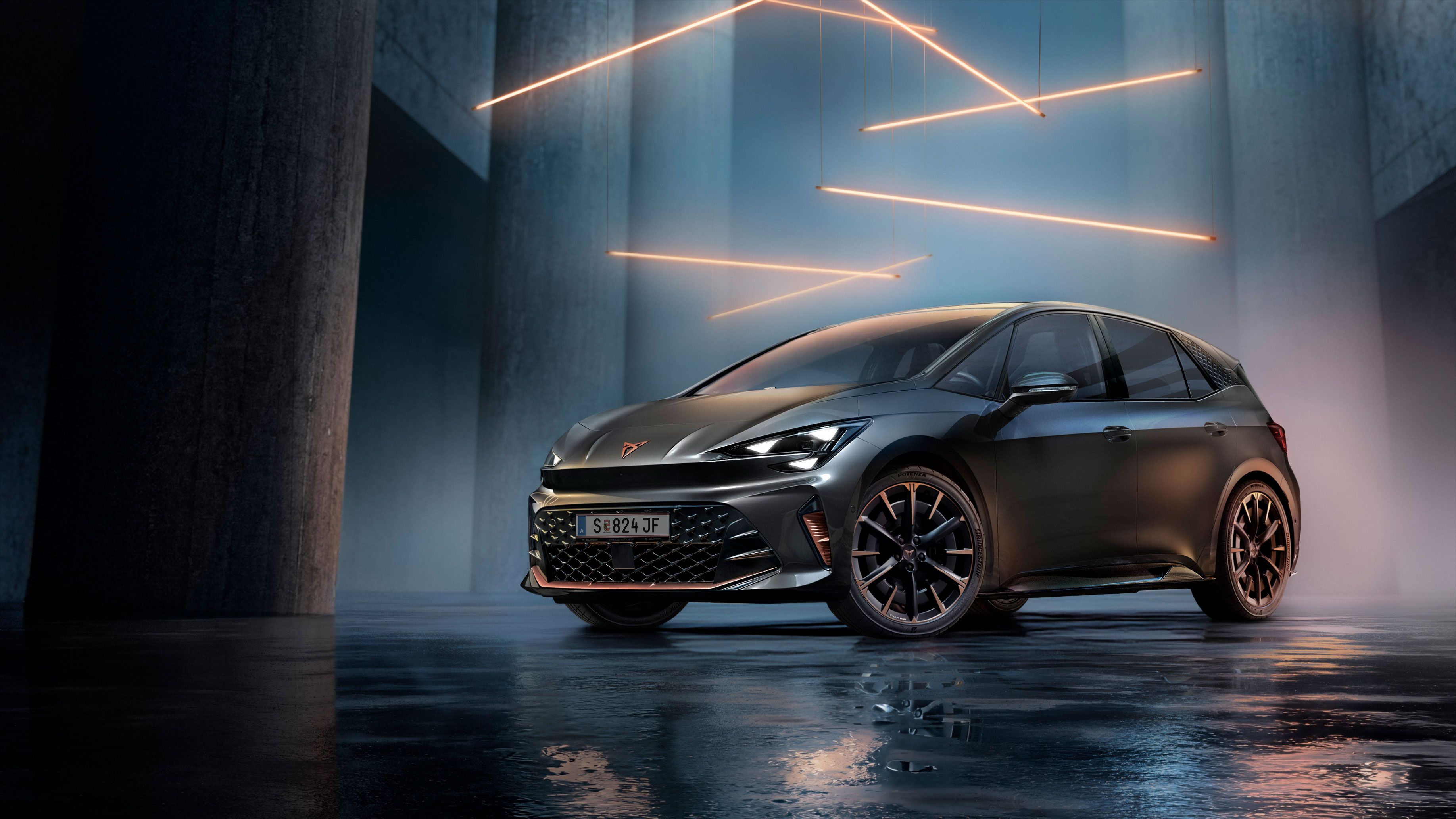 Sivé vozidlo CUPRA Born stojí v modernom, tmavom prostredí s vertikálnymi stĺpmi a svietiacimi LED pásmi. Podlaha je lesklá a odráža vozidlo aj osvetlenie. Auto pôsobí mohutne a elegantne.