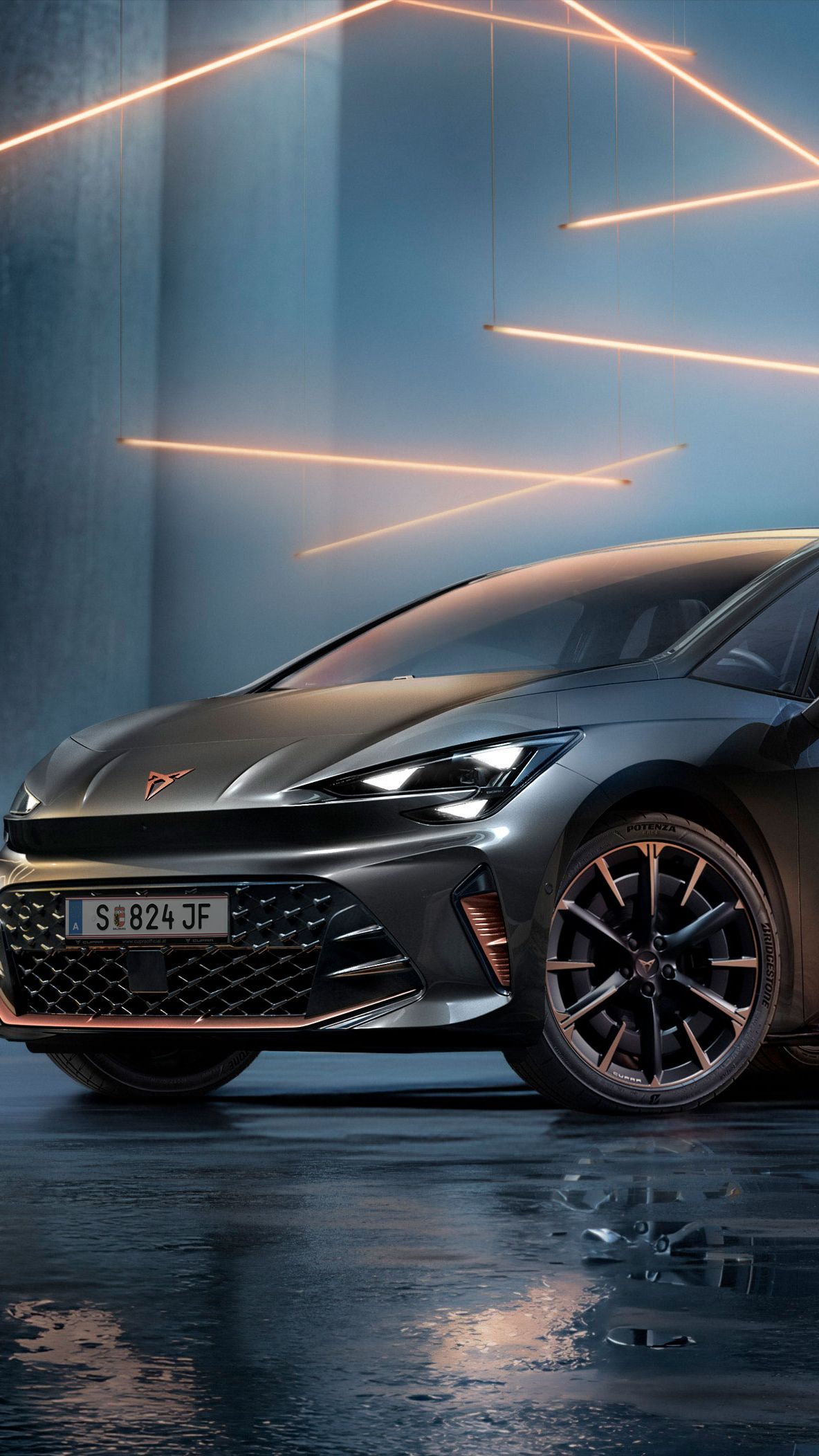 Sivé vozidlo CUPRA Born stojí v modernom, tmavom prostredí s vertikálnymi stĺpmi a svietiacimi LED pásmi. Podlaha je lesklá a odráža vozidlo aj osvetlenie. Auto pôsobí mohutne a elegantne.