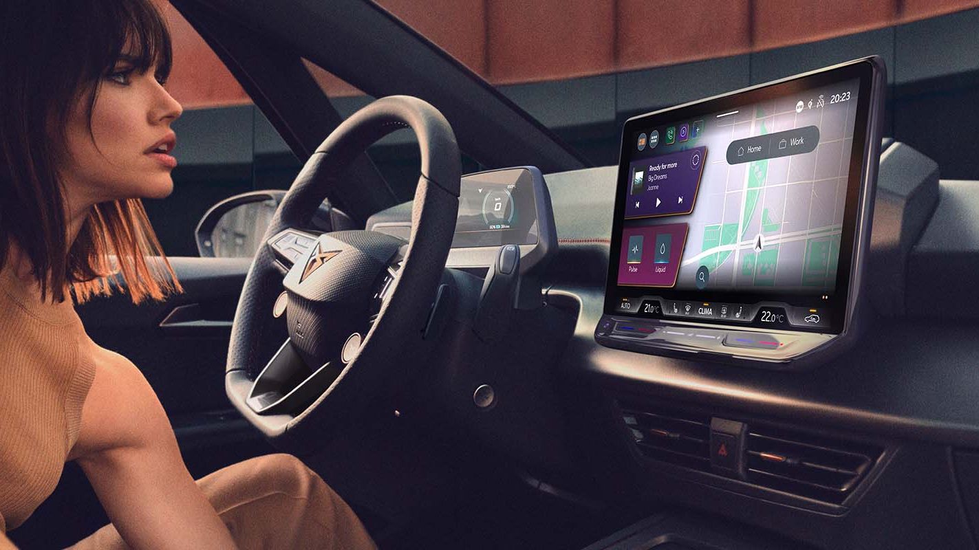 Žena sedí na sedadle vodiča a naťahuje sa. Na prednej palubnej doske sa nachádza veľká obrazovka so zobrazením navigácie.