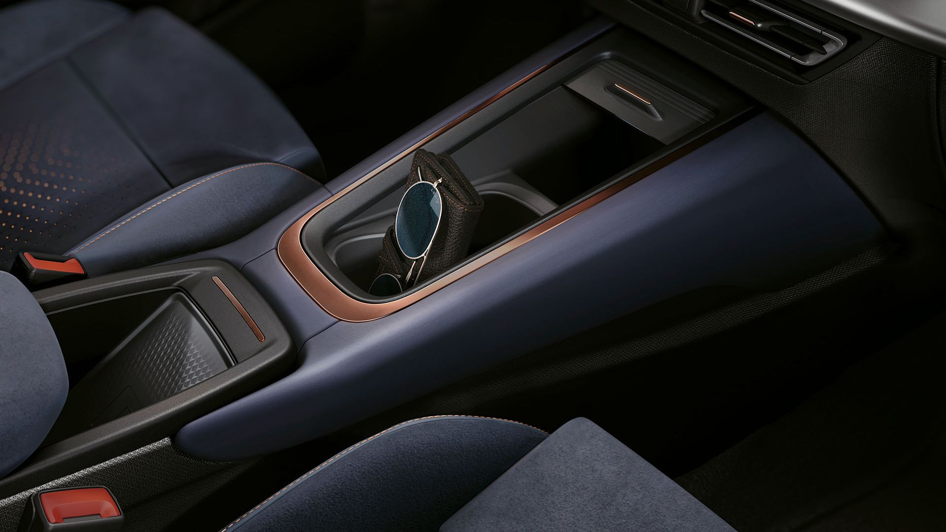 Detailný záber na interiér auta, konkrétne na stredovú konzolu. Viditeľný je držiak na poháre, ovládacie prvky klimatizácie a časť sedadla. Konzola má moderný dizajn s kombináciou modrej a medenej farby.