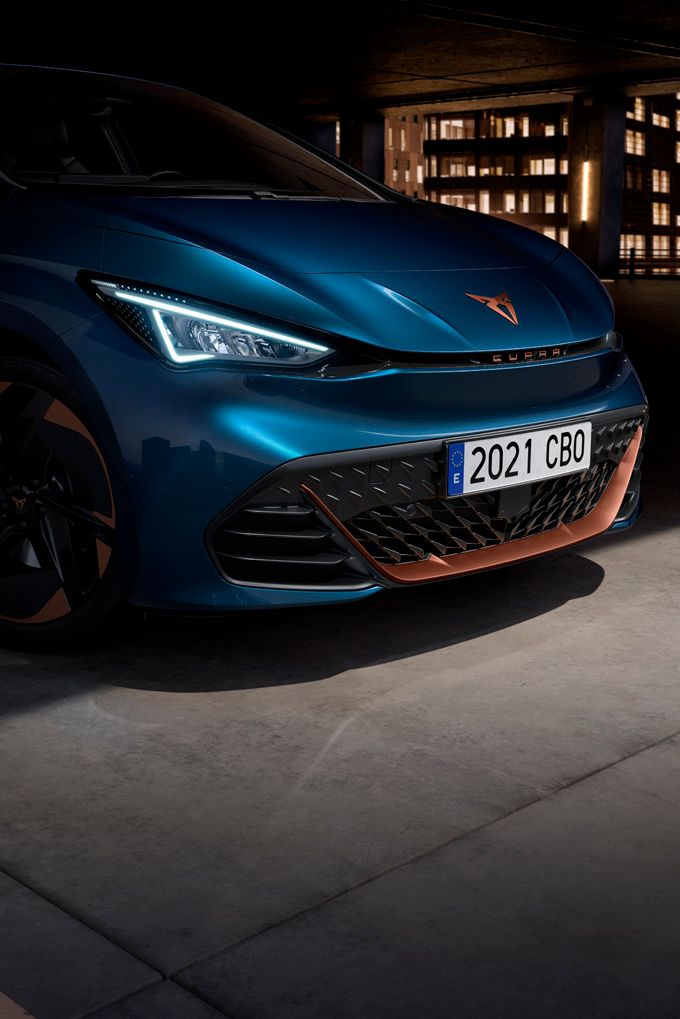 Modré auto zaparkované v garáži s osvetleným mestom v pozadí. Na ŠPZ je uvedený rok 2021. Predné svetlá auta sú zapnuté.