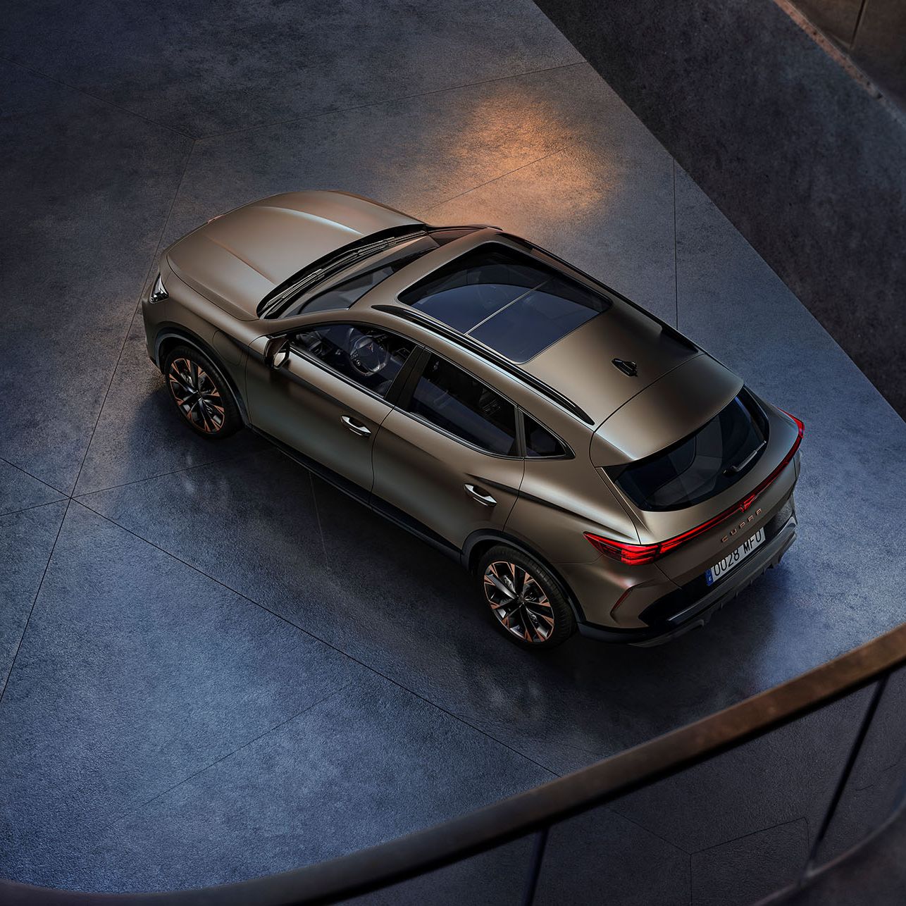Moderné hnedé SUV je zaparkované v tmavej miestnosti, pohľad zhora ukazuje jeho elegantné línie. Hladký povrch vozidla zdôrazňuje jeho moderný dizajn. Široké okná dávajú interiéru svetlý a vzdušný pocit.