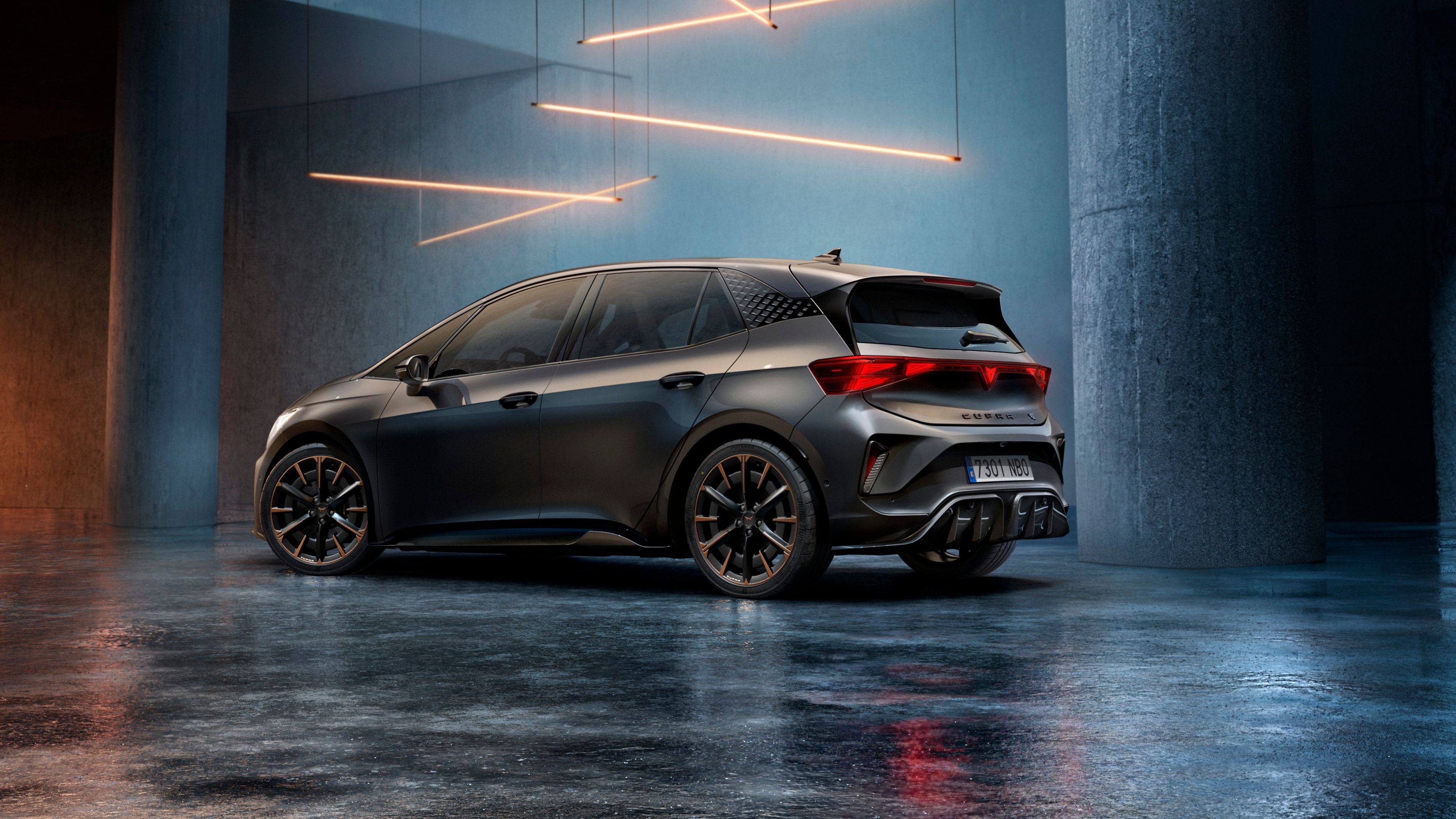 CUPRA Born stojí v štýlovo osvetlenom priemyselnom priestore s betónovými stenami a stĺpmi. Zo stropu visí niekoľko lineárnych svetelných zdrojov, ktoré vytvárajú elegantnú atmosféru. Vozidlo je vidieť zo zadnej strany a odráža svetlo na lesklej podlahe.