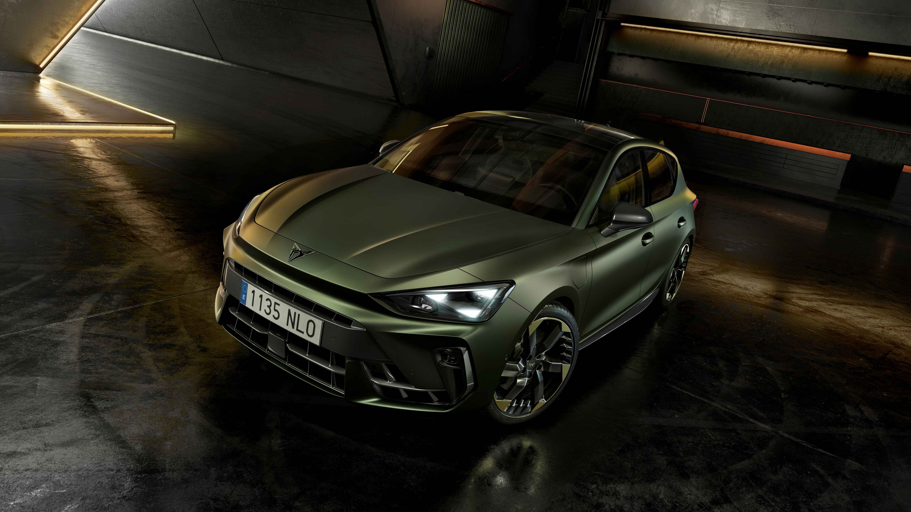 CUPRA Terramar v edícii Tribe v zelenej metalíze zaparkované v čiernom interiéri s dizajnovými LED lištami na stenách.