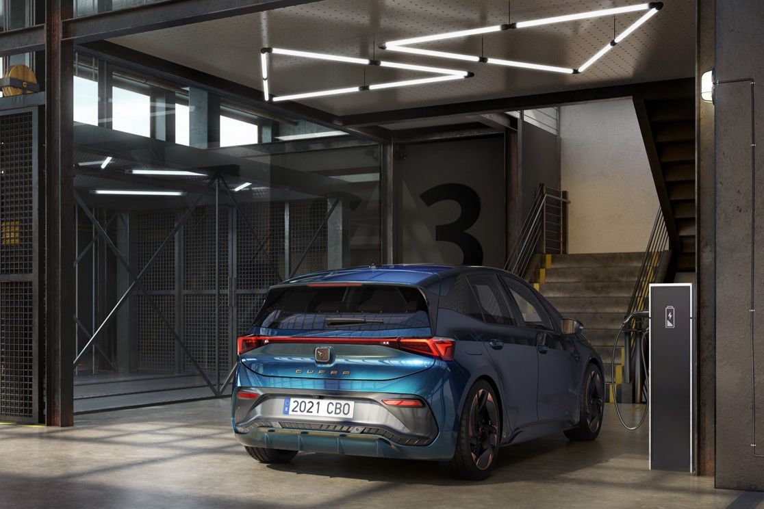 Modrý elektrický CUPRA Born je zaparkovaný v modernom parkovacom dome. Nabíja sa z nabíjacej stanice pri schodisku.