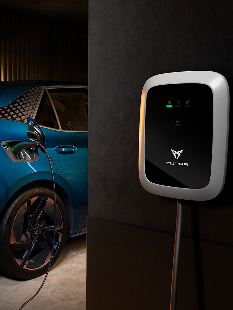 Nabíjacia stanica CUPRA je pripojená k modrému elektrickému autu cez nabíjací kábel v garáži. Nabíjacia stanica zobrazuje stav nabíjania pomocou LED diód.