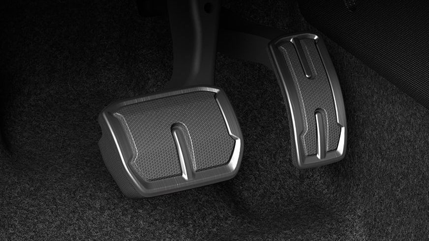 Detailný záber na pedále automobilu. Zobrazený sú plynový a brzdový pedál na pozadí tmavého koberca.