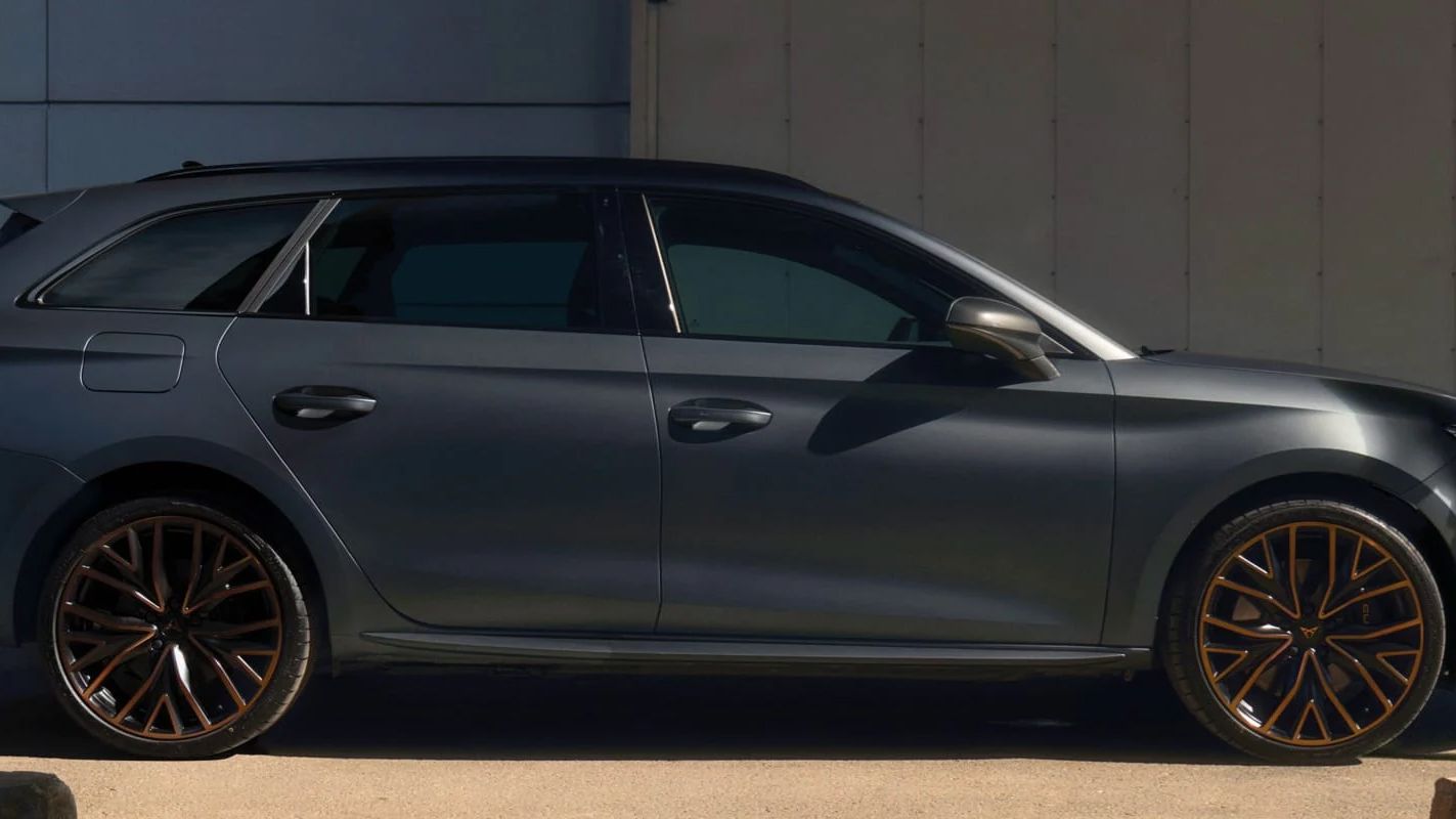 Muž stojí vedľa sivého CUPRA Leon Sportstourer zaparkovaný pred modernou budovou, drží v ruke tablet a má oblečený športový outfit. Pozadie je minimalistické s niekoľkými kovovými prvkami.