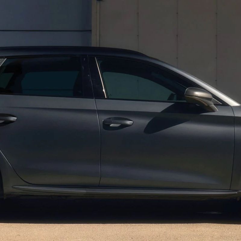 Muž stojí vedľa sivého CUPRA Leon Sportstourer zaparkovaný pred modernou budovou, drží v ruke tablet a má oblečený športový outfit. Pozadie je minimalistické s niekoľkými kovovými prvkami.