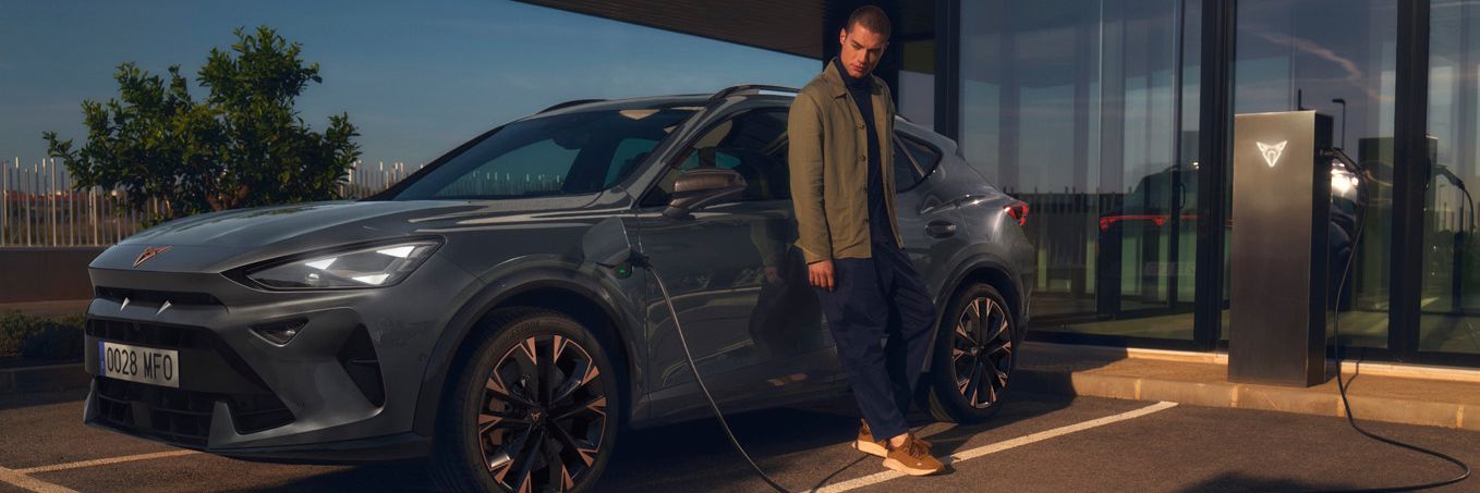 CUPRA Formentor e-Hybrid pri nabíjaní pred modernou budovou. Muž sa opiera o vozidlo.