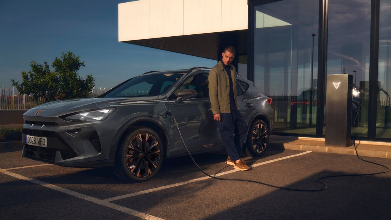 CUPRA Formentor e-Hybrid pri nabíjaní pred modernou budovou. Muž sa opiera o vozidlo.