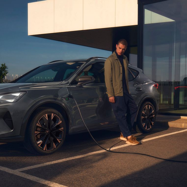 CUPRA Formentor e-Hybrid pri nabíjaní pred modernou budovou. Muž sa opiera o vozidlo.