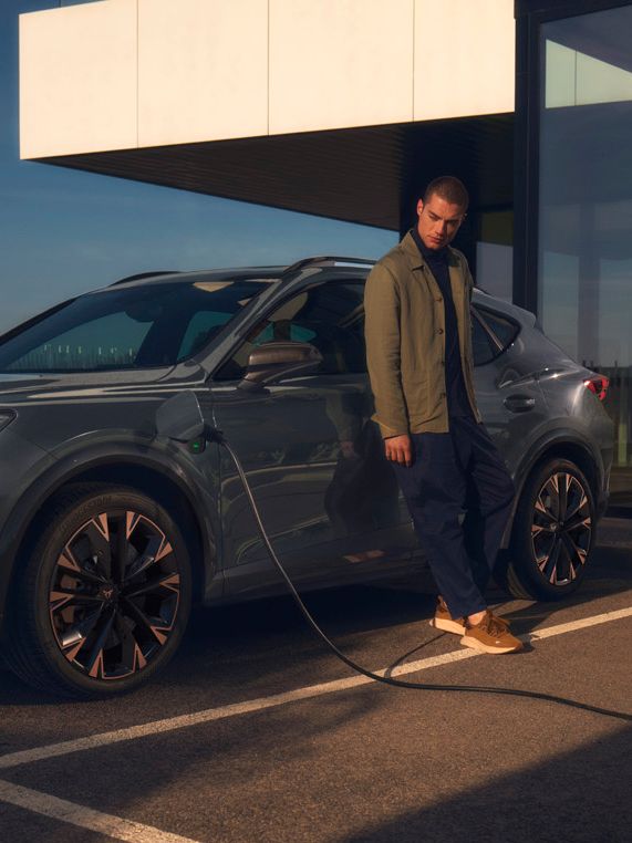 CUPRA Formentor e-Hybrid pri nabíjaní pred modernou budovou. Muž sa opiera o vozidlo.