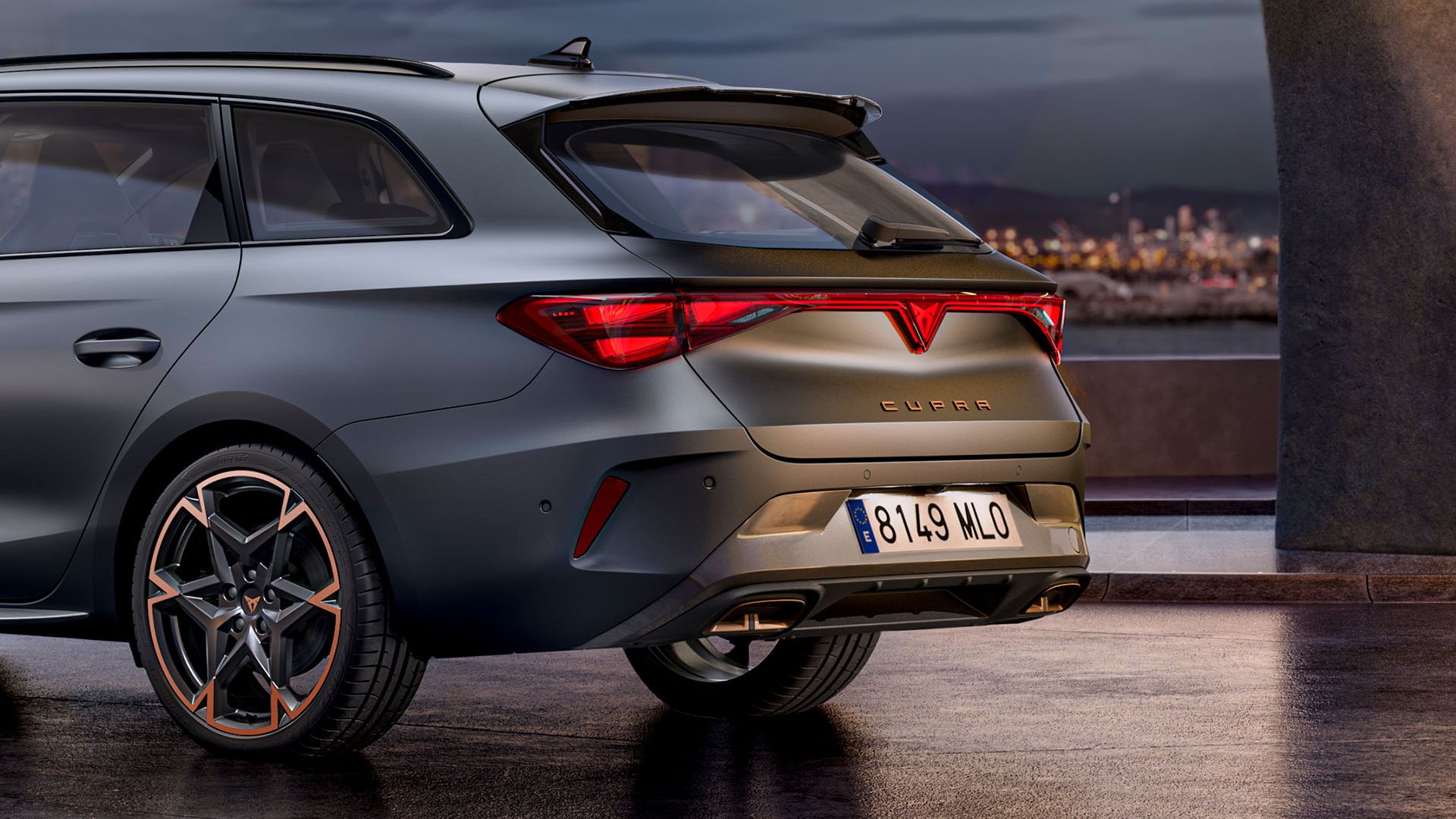 CUPRA Leon Sportstourer je zaparkované na voľnej ploche s výhľadom na mesto. Svetlá mesta sú rozmazané. Na aute sú elegantné disky s bronzovými detailmi.