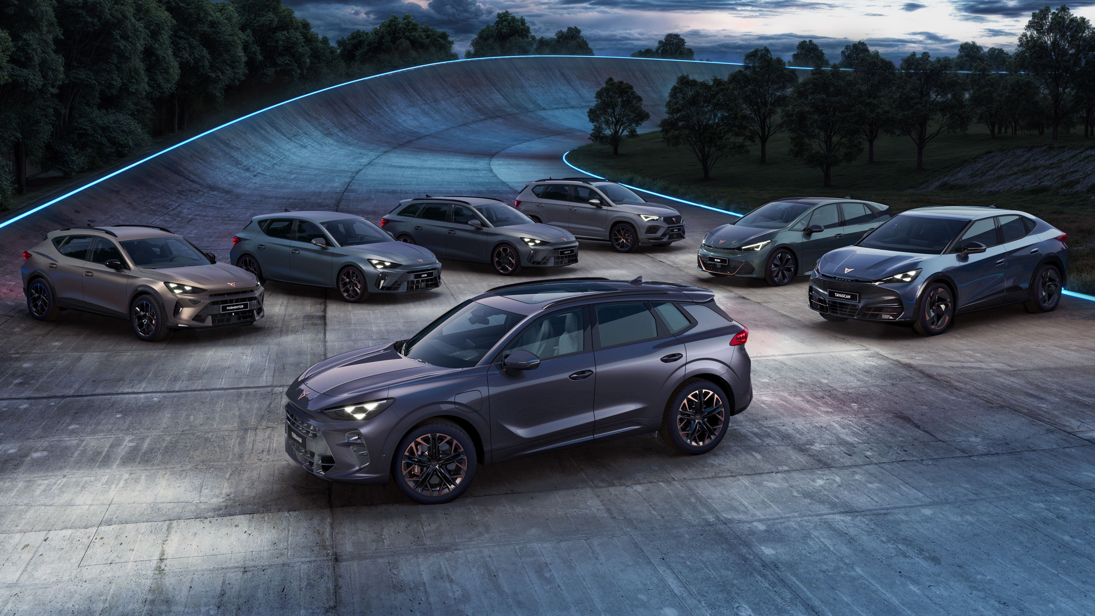 Pohľad na sedem športových vozidiel CUPRA , postavených na závodnej dráhe počas súmraku. Auta majú šedú farbu a sú to rôzne modely. Okolie je lemované stromami a osvetlené modrými svetlami.