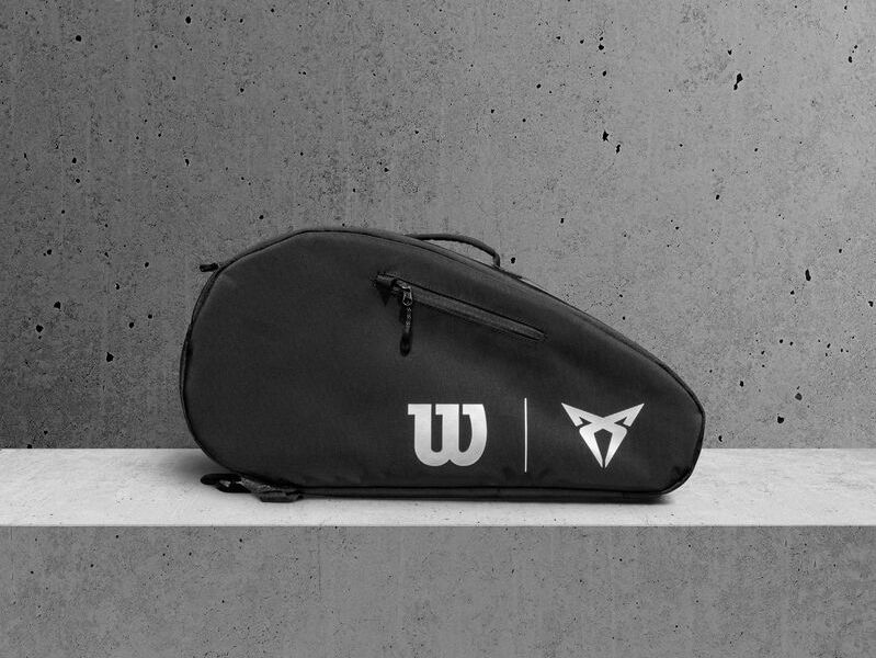 Čierna taška značky Wilson s logom CUPRA opretá o betónovú stenu. Taška má jedno veľké vrecko na zips.