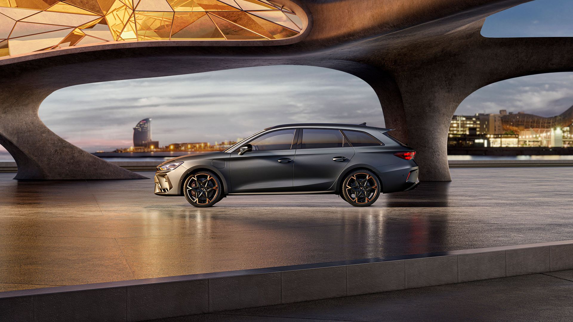 CUPRA Leon Sportstourer stojí na modernom námestí pri umeleckej architektúre. Priestor osvetľuje sklenená strecha, ktorá vytvára zaujímavé svetelné efekty. V pozadí sú budovy a mestská scenéria.