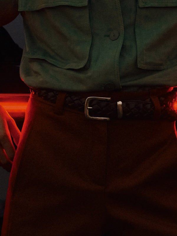 Pohľad zozadu na čierne auto so zapnutými výraznými červenými zadnými svetlami. Pred autom stojí muž v zelenej košeli a hnedých nohaviciach s rukami opretými o vozidlo. 