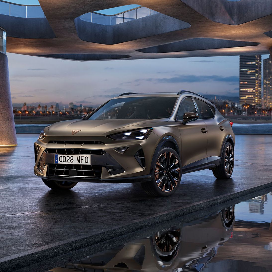 Moderné SUV sa nachádza pod futuristickým, architektonicky zaujímavým mostom vedľa stĺpov za súmraku. V pozadí je panoráma mesta. Auto je zaparkované na mokrej dlažbe, v ktorej sa odráža jeho obraz.