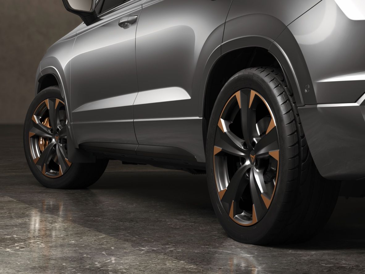 Strieborné SUV zaparkované na lesklom mramore. Zadná časť vozidla a kolesá s bronzovými akcentmi sú v popredí. Na pozadí je tmavá stena.