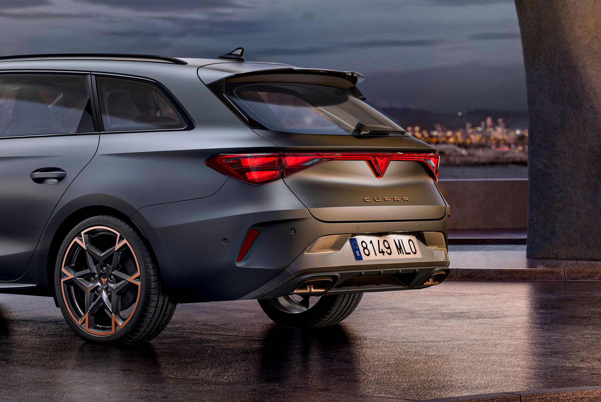 CUPRA Leon Sportstourer je zaparkované na voľnej ploche s výhľadom na mesto. Svetlá mesta sú rozmazané. Na aute sú elegantné disky s bronzovými detailmi.