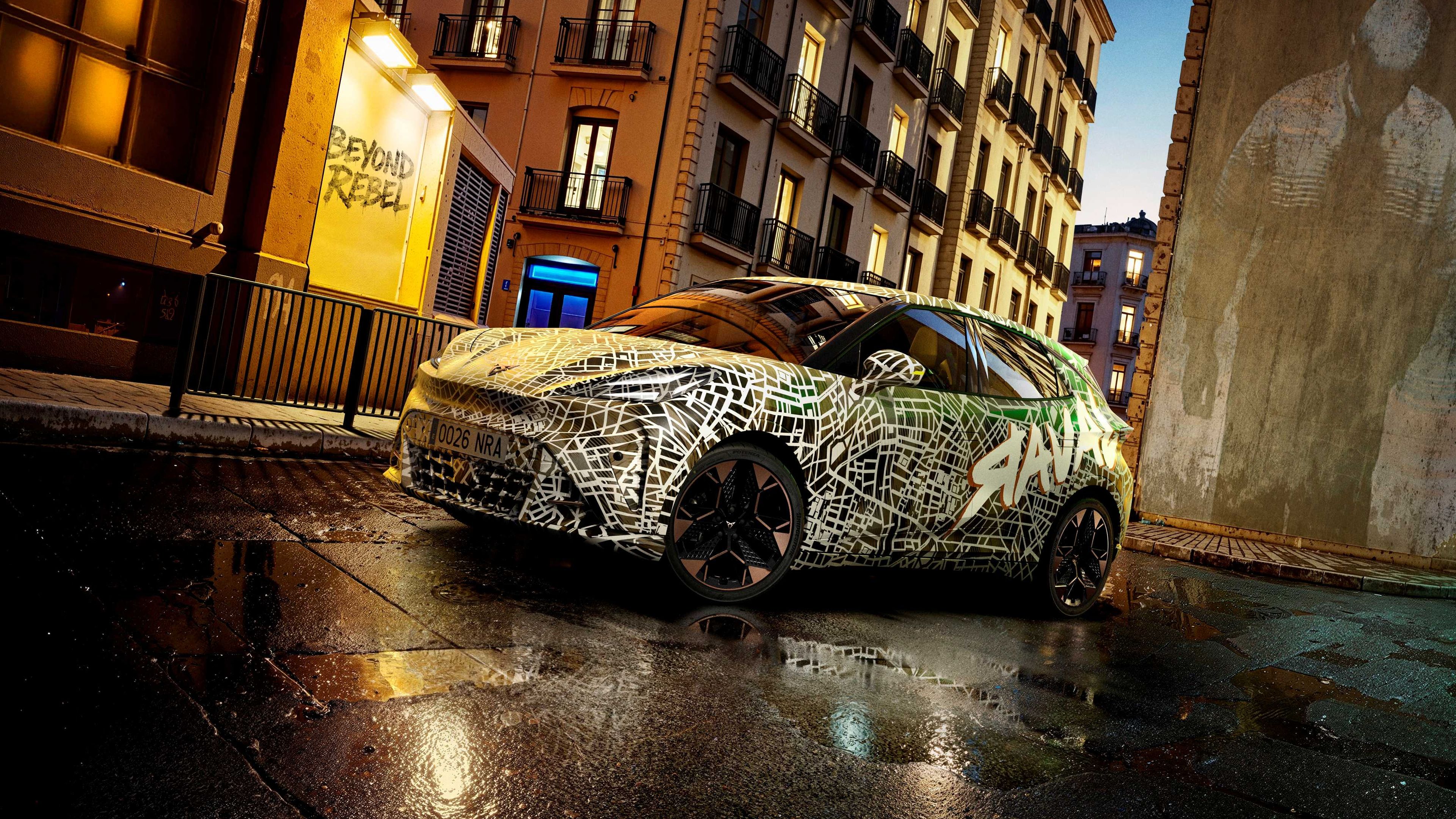 Kamuflovaný model CUPRA stojí na mokrej ceste pred historickou budovou za súmraku.