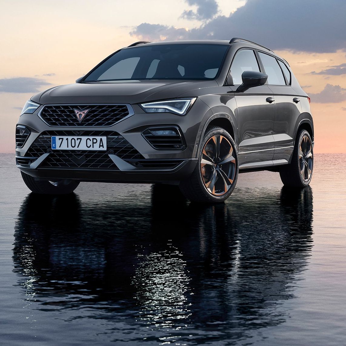 SUV značky Cupra stojí na povrchu vody pri západe slnka. Pozadie je zahalené do jemných odtieňov ružovej a modrej. Skvelý odraz vozidla na vode dodáva scéne pokojný a pôsobivý efekt.