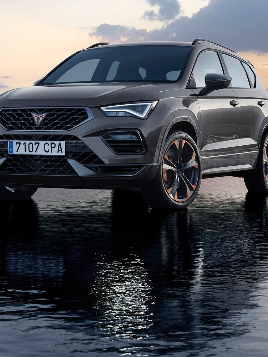 SUV značky Cupra stojí na povrchu vody pri západe slnka. Pozadie je zahalené do jemných odtieňov ružovej a modrej. Skvelý odraz vozidla na vode dodáva scéne pokojný a pôsobivý efekt.