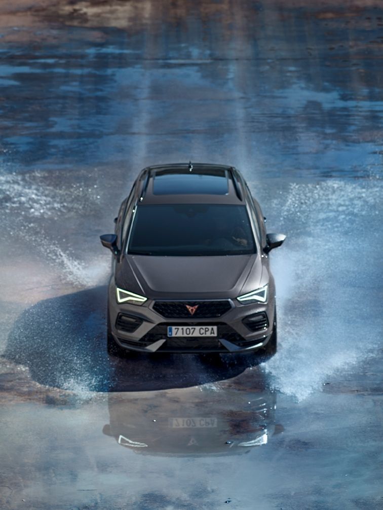 Auto Cupra Ateca prechádza cez vodu. Predné svetlá sú rozsvietené.