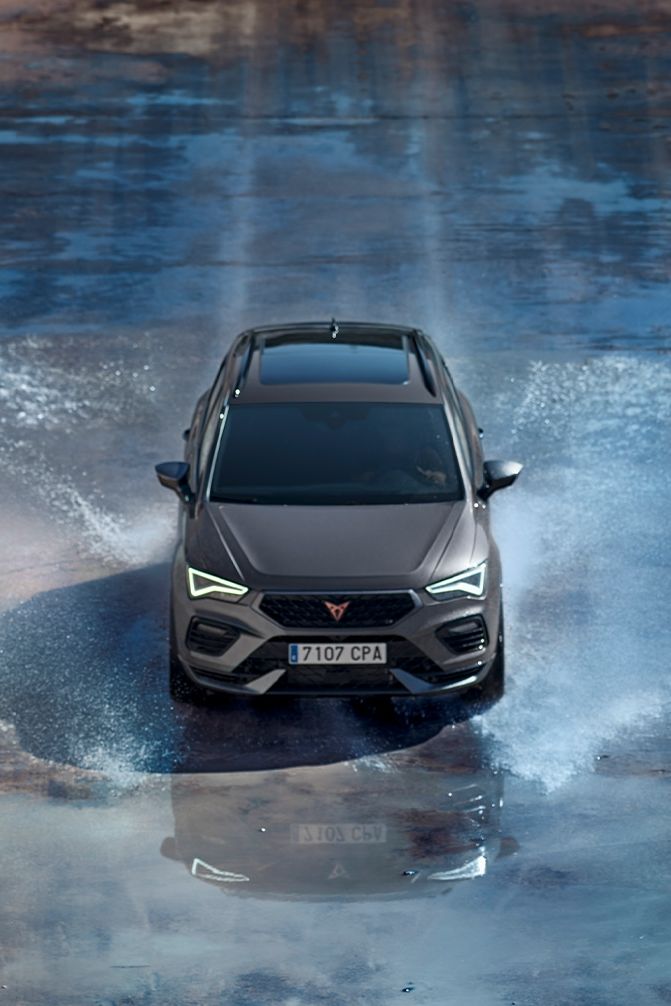 Auto Cupra Ateca prechádza cez vodu. Predné svetlá sú rozsvietené.
