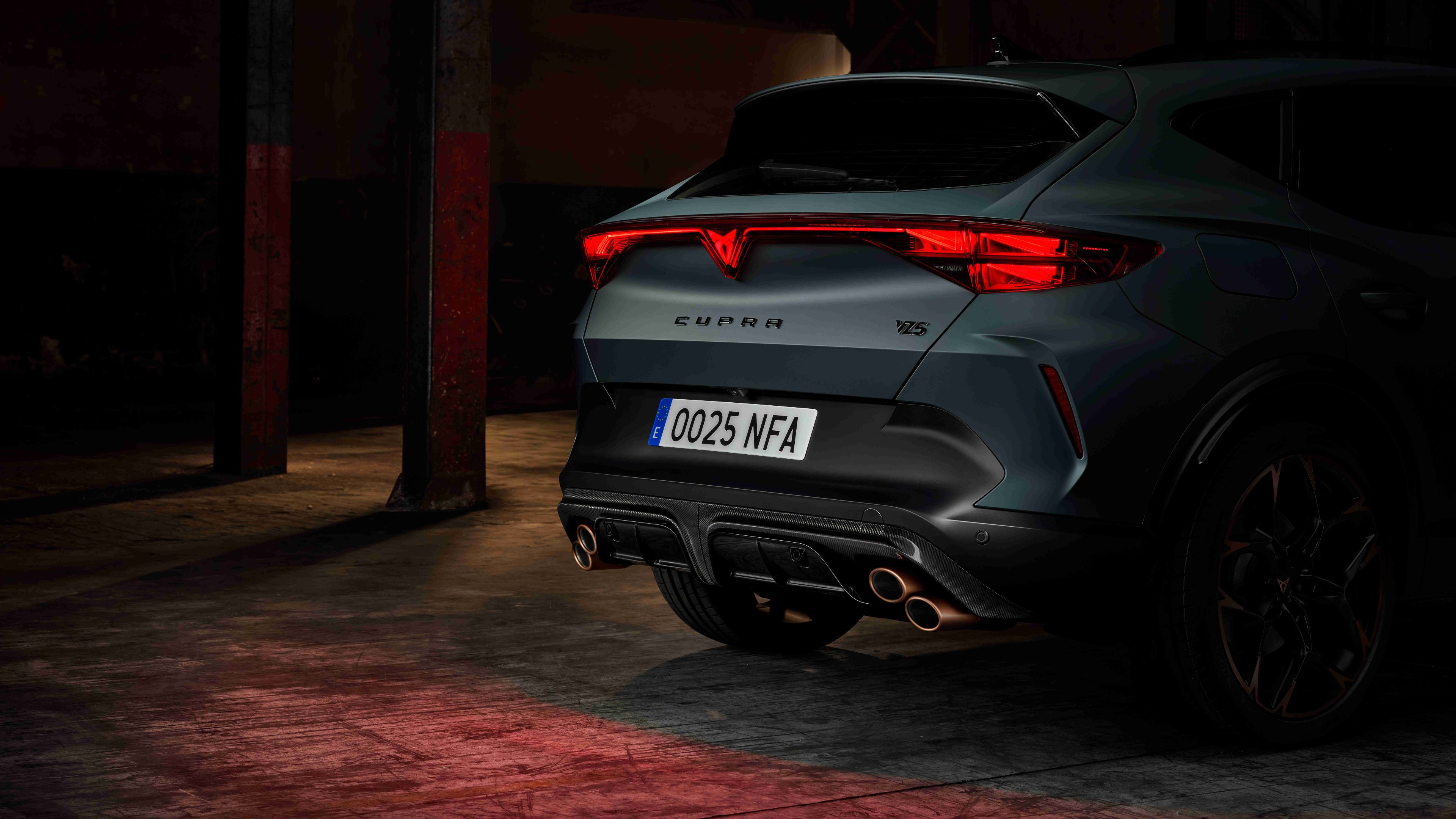 Tmavo zelené športové auto Cupra s červenými svetlami, zaparkované v priemyselnej budove. 