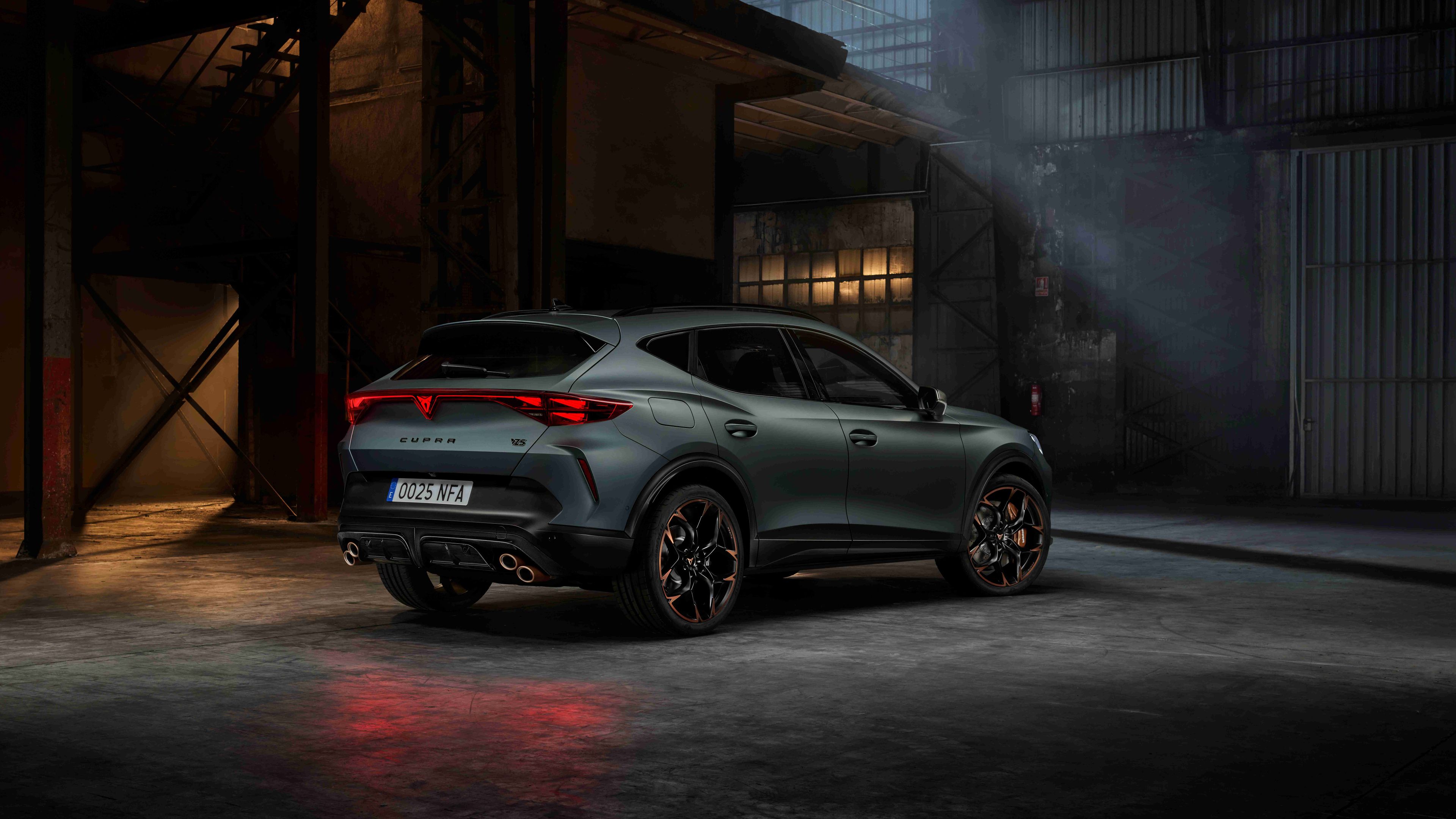 Moderný Cupra Formentor zaparkovaný v industriálnom priestore. Auto je zelené, má športový dizajn a výrazné LED svetlá na zadnej časti. 