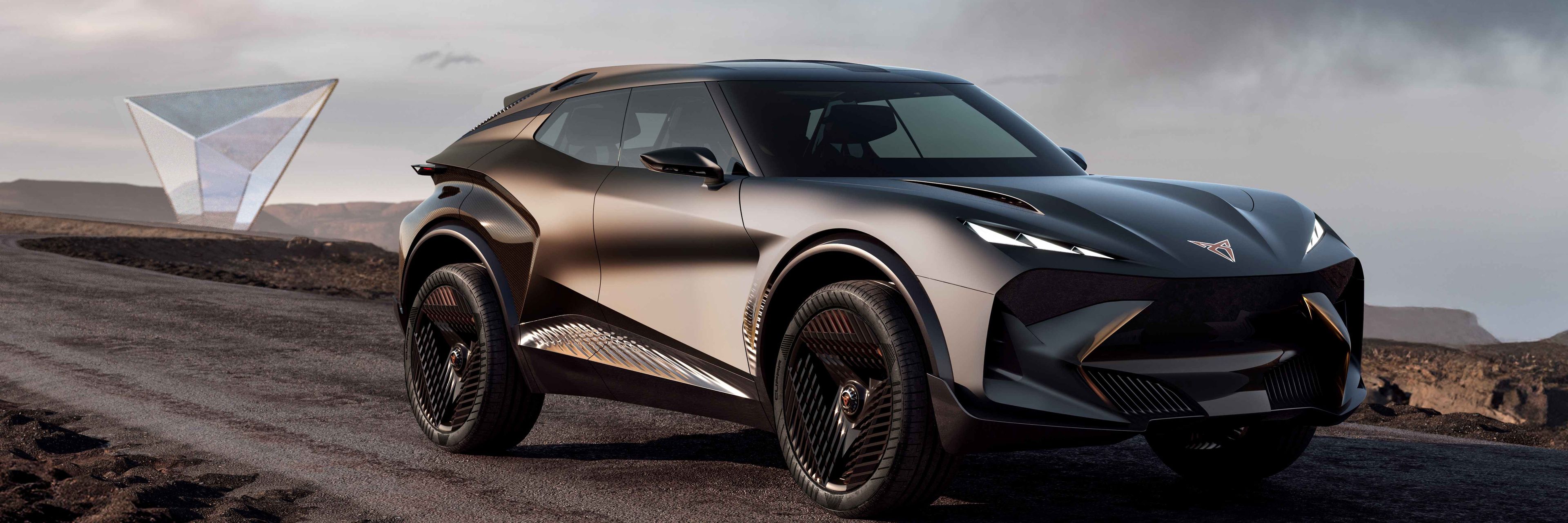 Moderné, športové SUV na prašnej ceste. Auto má zlato-čierny odtieň a futuristický dizajn. V pozadí sa nachádza priehľadný geometrický objekt a skalnatá krajina.