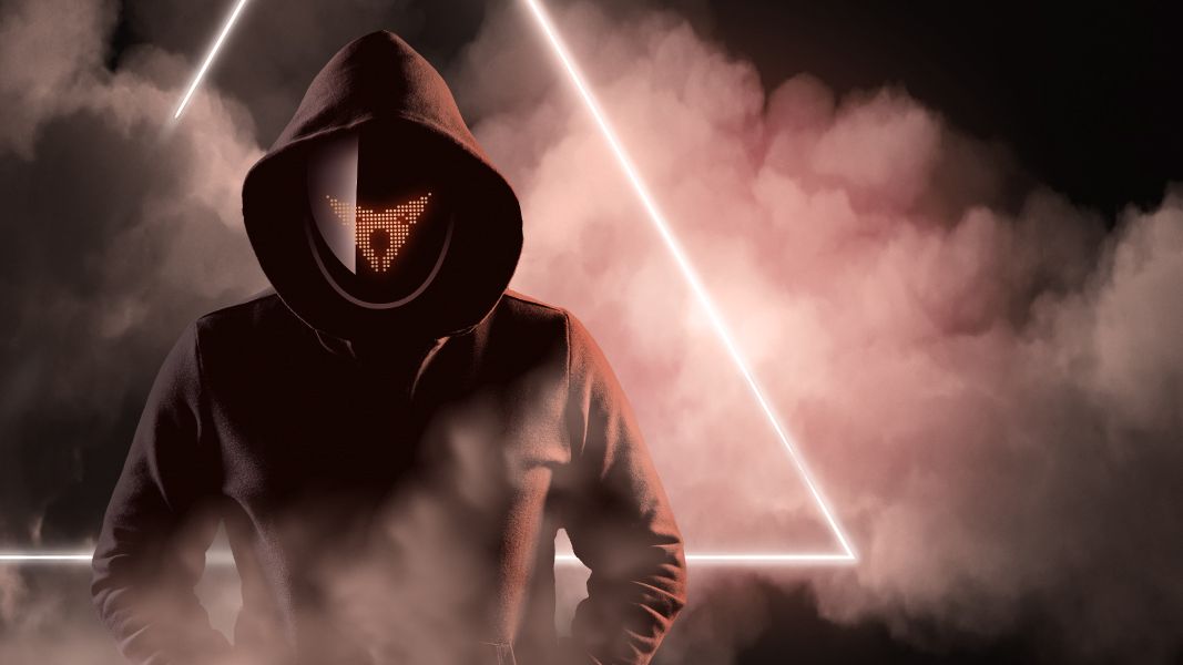 Osoba v tmavej mikine s kapucňou stojí pred svetelným trojuholníkom, ktorý je obklopený hmlou. Nie je vidieť celú tvár, len masku s logom CUPRA a kapucňu. Atmosféra pôsobí tajomne.