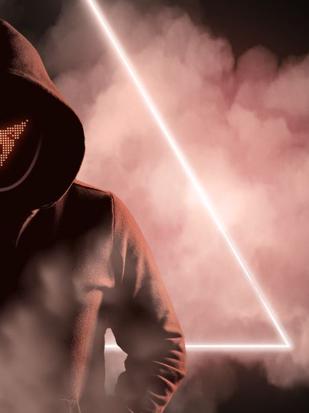 Osoba v tmavej mikine s kapucňou stojí pred svetelným trojuholníkom, ktorý je obklopený hmlou. Nie je vidieť celú tvár, len masku s logom CUPRA a kapucňu. Atmosféra pôsobí tajomne.