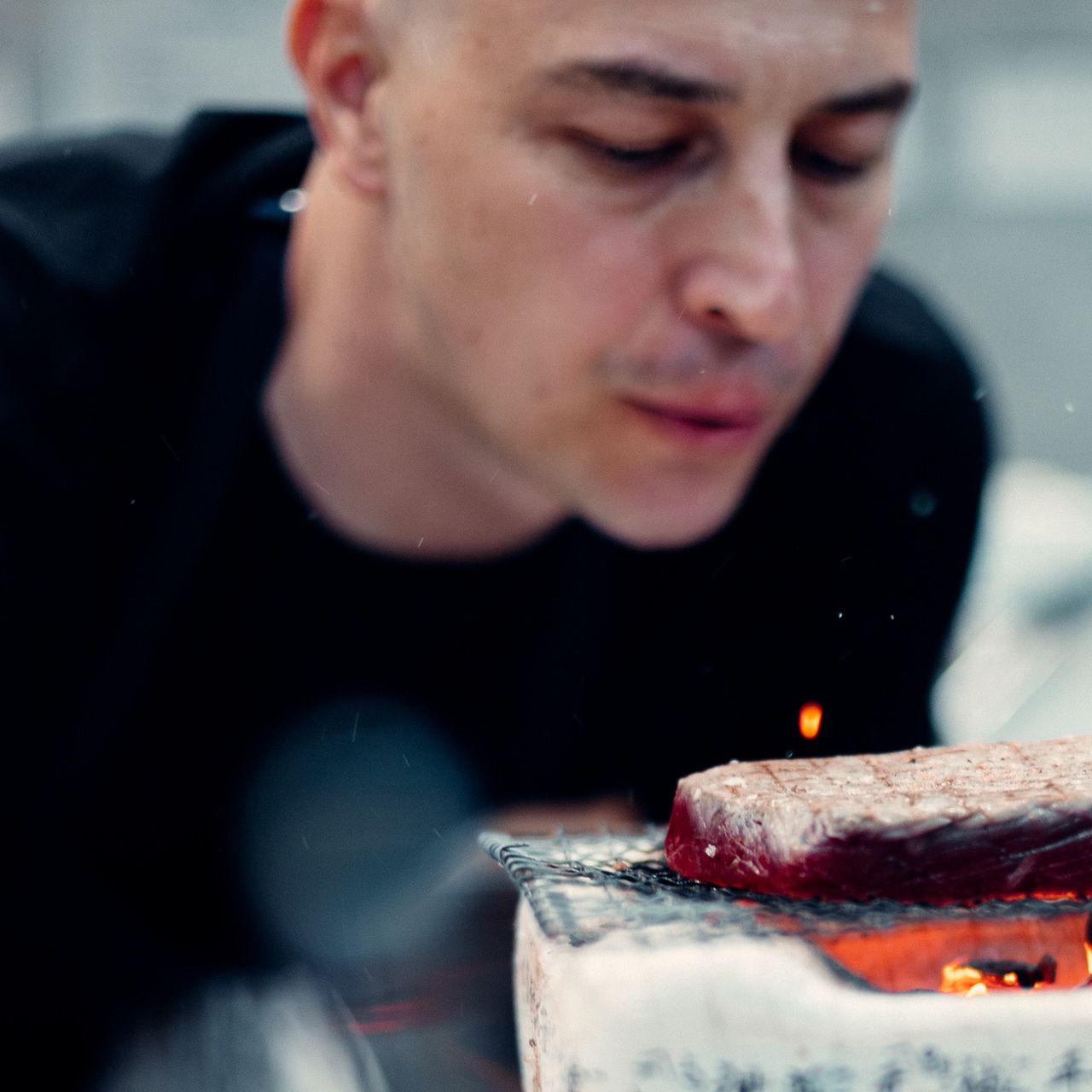 Kus mäsa sa griluje na ohni, pričom v pozadí je kuchár. Gril je umiestnený v interiéri.