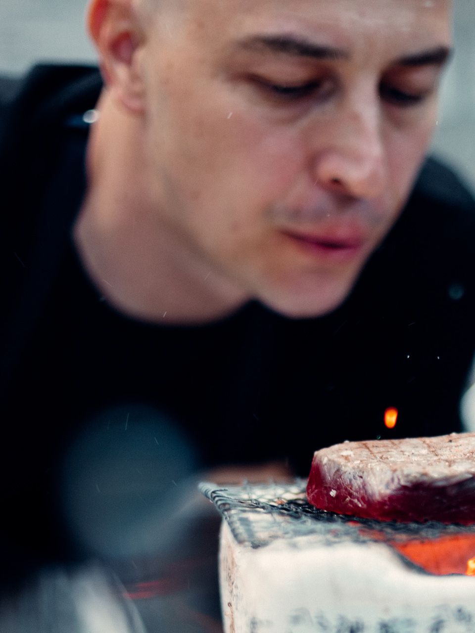 Kus mäsa sa griluje na ohni, pričom v pozadí je kuchár. Gril je umiestnený v interiéri.