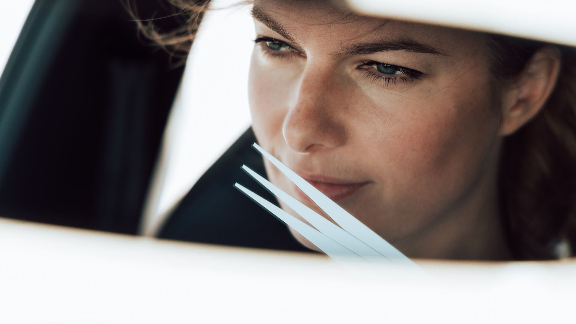 Žena sedí v aute. Má hnedé vlasy. Jej obraz zreteľne vidieť v spätnom zrkadle.