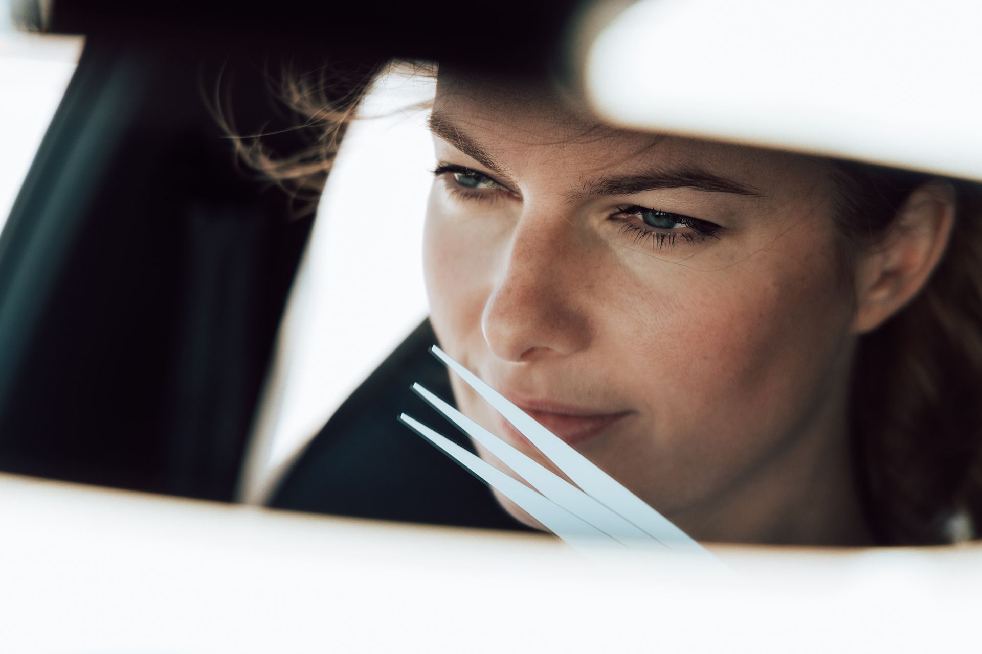 Žena sedí v aute. Má hnedé vlasy. Jej obraz zreteľne vidieť v spätnom zrkadle.