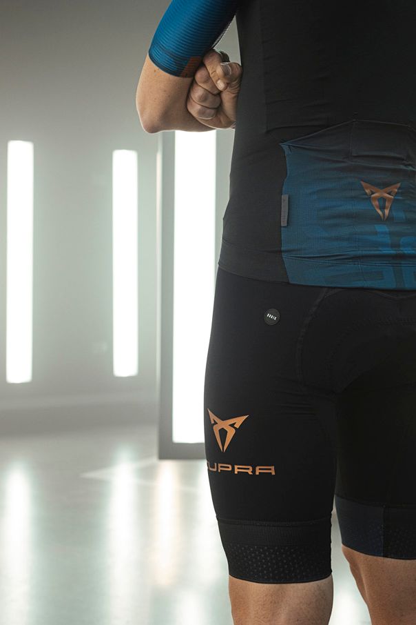 Osoba stojí v bielej modernej miestnosti s úzkymi vysokými oknami bez zariadenia má na sebe športové oblečenie značky Q36.5 s logami CUPRA.