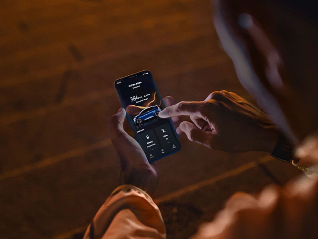 Človek ovláda smartfón, ktorý zobrazuje informácie o vozidle, vrátane jeho batérie a ďalších nastavení. Prostredie nočného osvetlenia naznačuje, že je večer alebo noc.