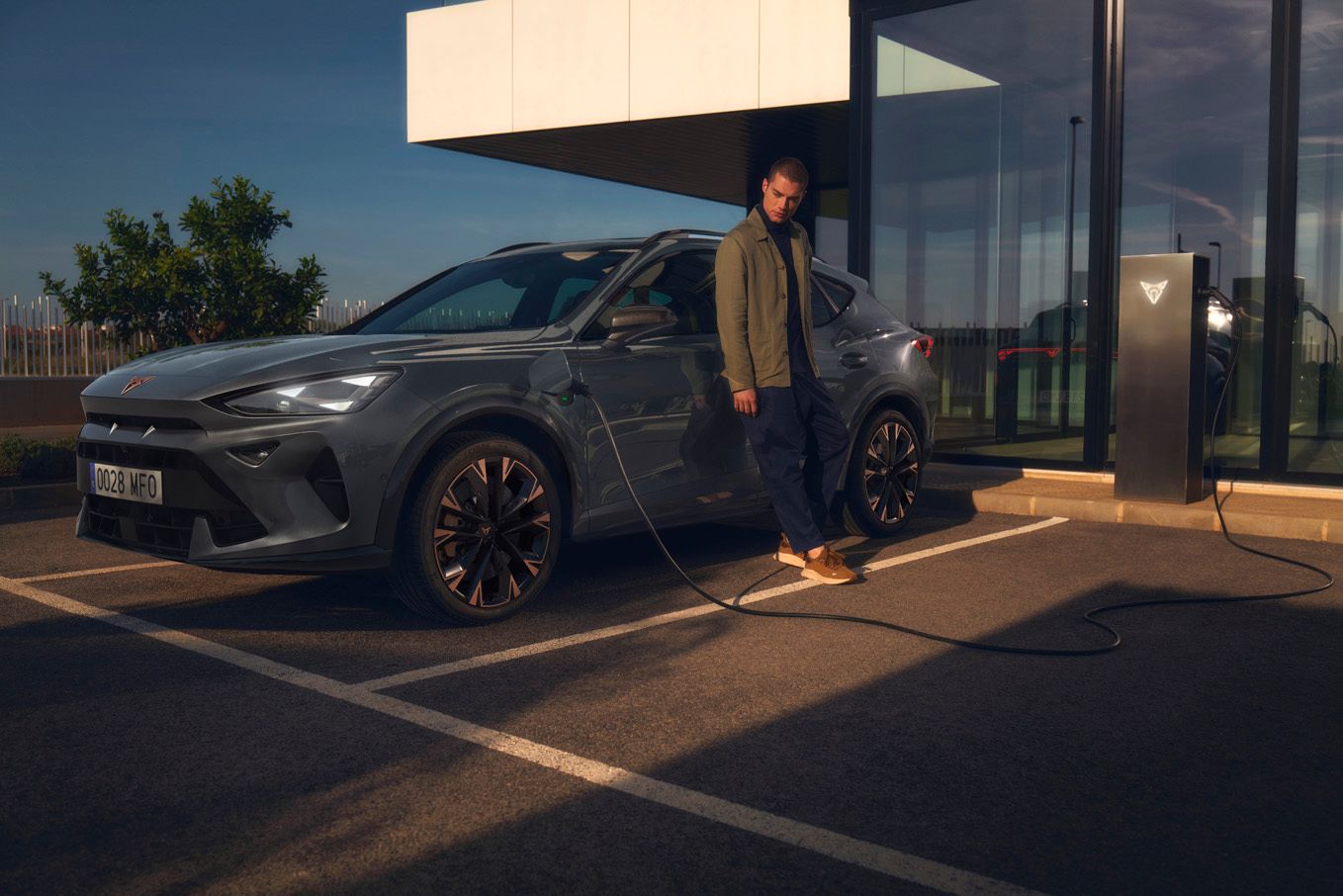 CUPRA Formentor e-Hybrid pri nabíjaní pred modernou budovou. Muž sa opiera o vozidlo.