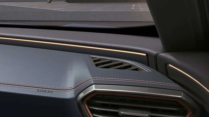 Detail na interiér auta, konkrétne na pravú stranu palubnej dosky s ventilačným otvorom. Na palubnej doske je vidieť nápis "Airbag". Pozadie je tmavé a palubná doska má elegantné prešívanie.