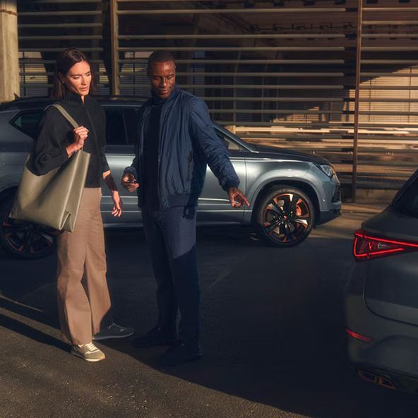 Muž a žena na parkovisku pred showroomom sa pozerajú na vozidlá CUPRA.